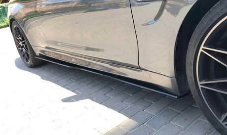 A sleek car with glossy dark wheels is parked, reflecting sunlight on its shiny surface, situated on a paved area.