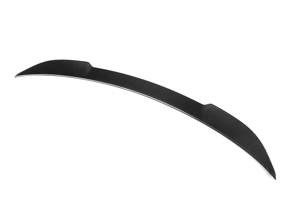 A black carbon fiber car spoiler, shaped with a sleek, aerodynamic curve, rests isolated against a plain white background.