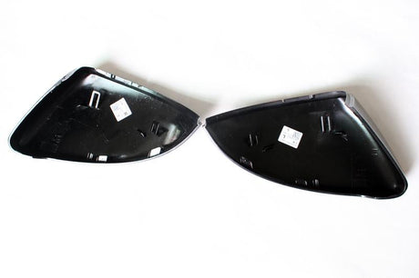 Two black plastic car mirror covers lie open on a white surface, with stickers displaying product information on each cover's interior.