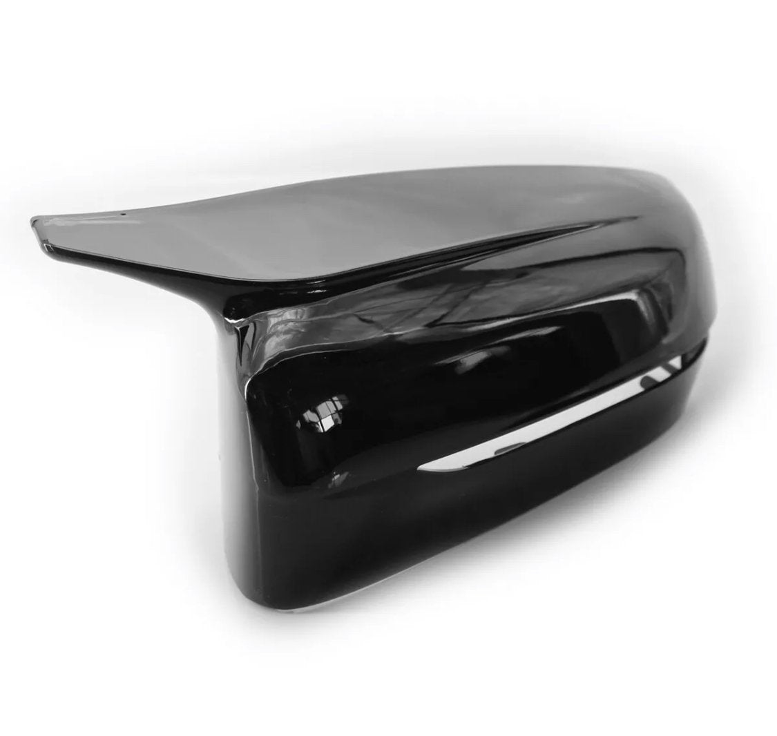 A glossy black car side mirror cover rests on a plain white background, reflecting light and displaying smooth, aerodynamic contours.