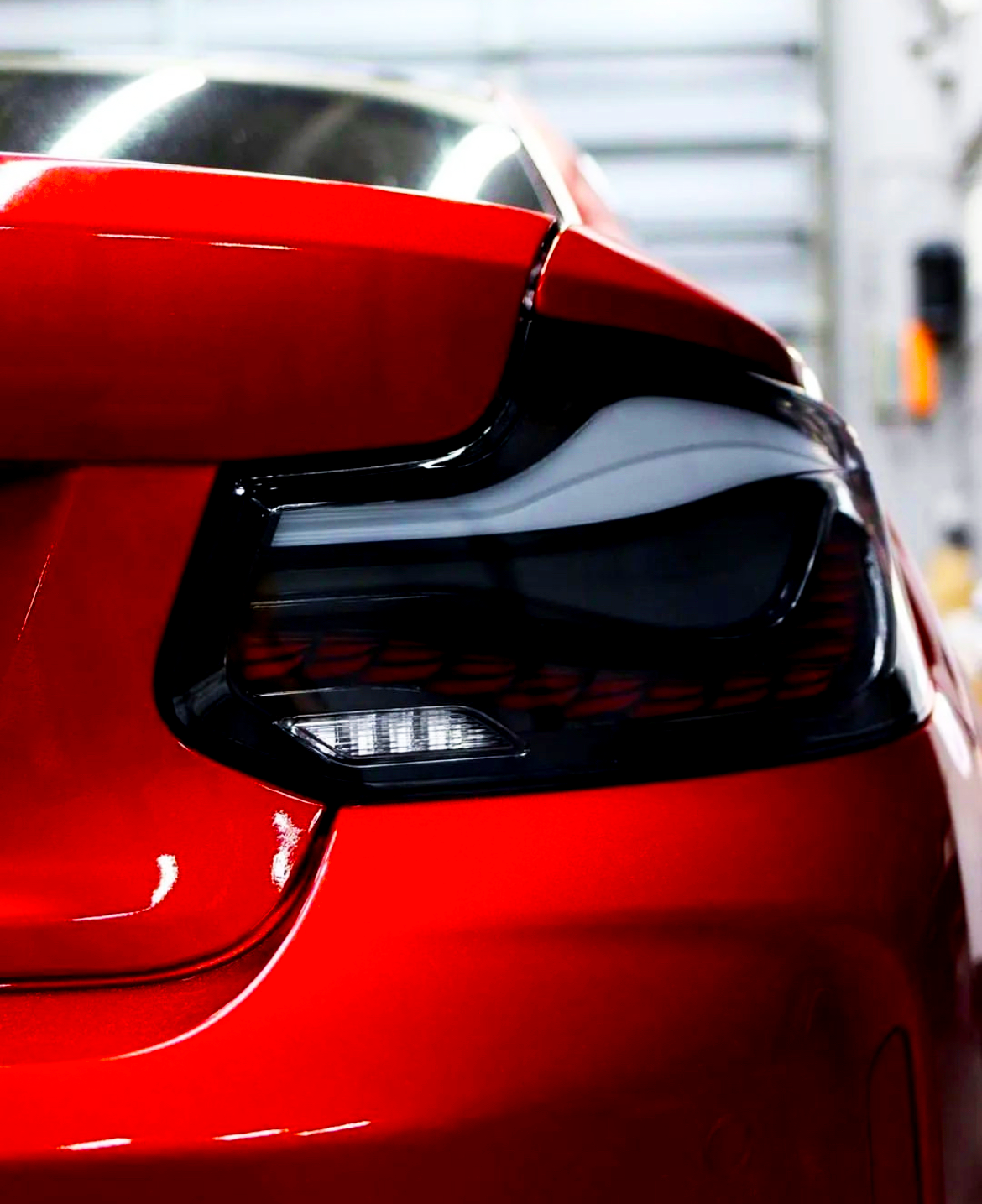 A red car's rear taillight, inactive, displayed in a brightly lit indoor garage setting, highlighting sleek curves and glossy finish.