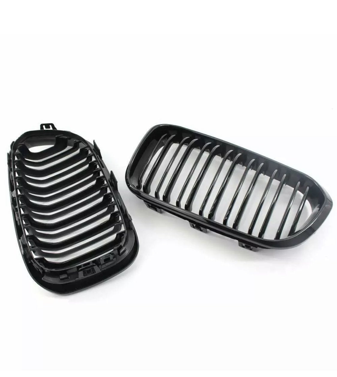 Two black car grille parts, each with parallel vertical slats, are positioned side by side. They are set against a plain, white background.