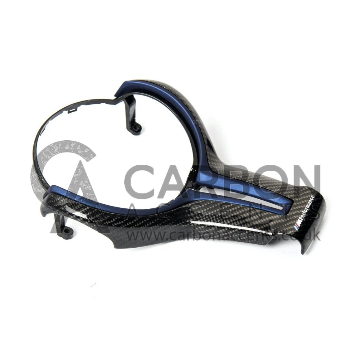 A carbon fiber car steering wheel trim with a blue accent rests on a plain surface. Text reads "M Performance" and a watermark "CARBON ACCENTS www.carbonaccents.co.uk" overlays the image.
