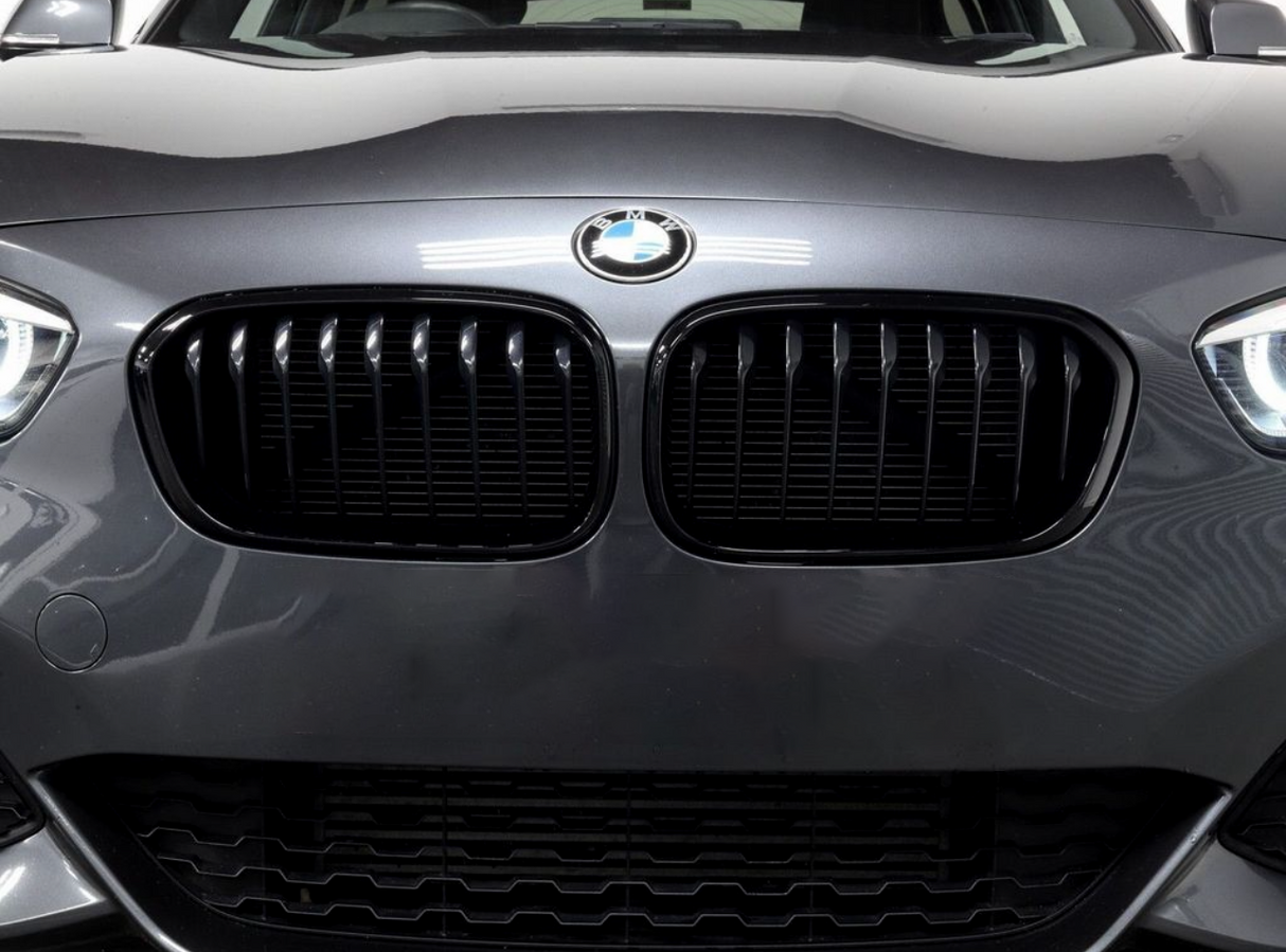 Car grille with vertical slats, featuring a BMW logo above, is prominently displayed on a dark gray vehicle in a well-lit indoor setting.