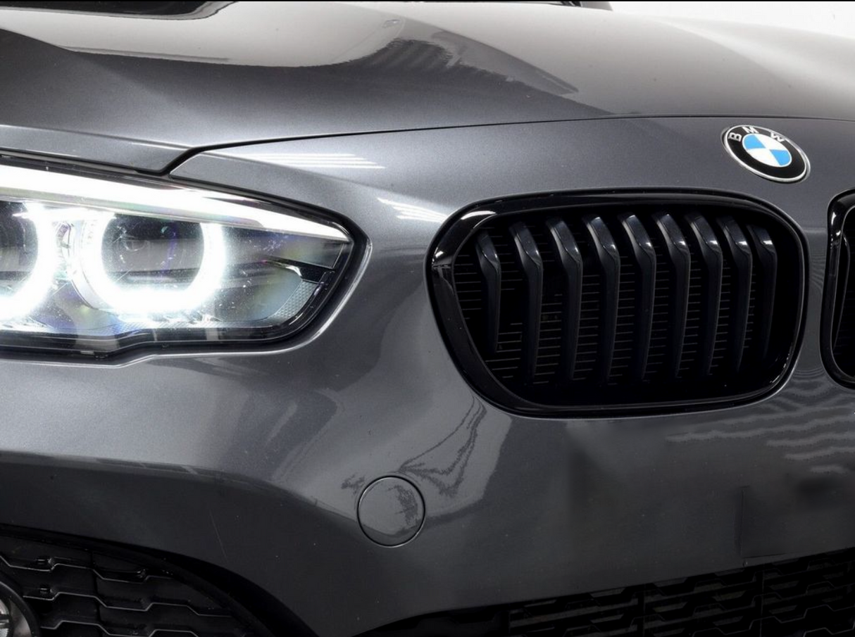 A car's front features illuminated headlights and a black kidney grille, with a BMW emblem on the hood, set in a glossy, grey exterior.