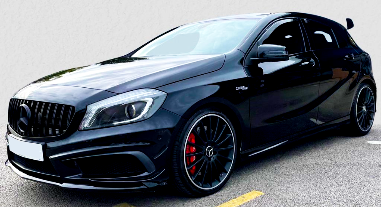 A sleek, black Mercedes-Benz hatchback with sporty, red brake calipers is parked on asphalt. It has a distinctive front grille and the emblem "Turbo 4MATIC" on the side.