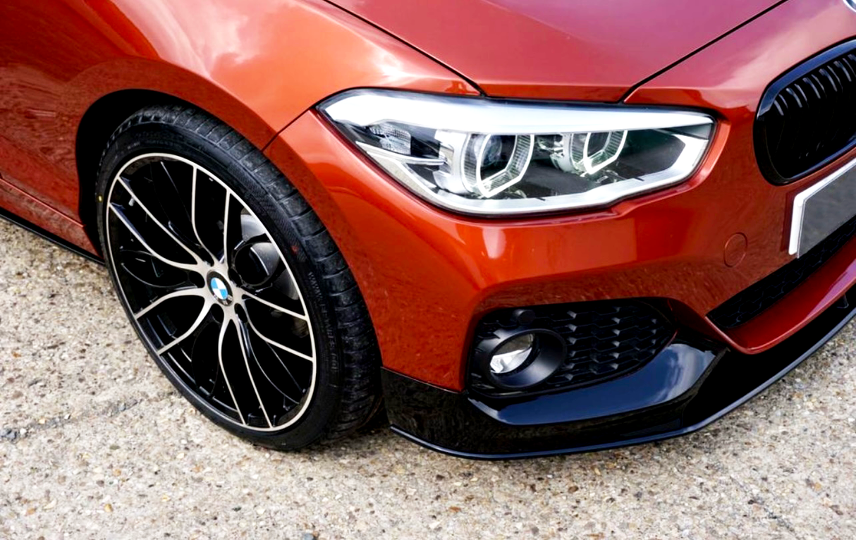 A red car displays its sleek front, showcasing dynamic headlights and stylish black alloy wheels, parked on a textured, light-colored pavement.