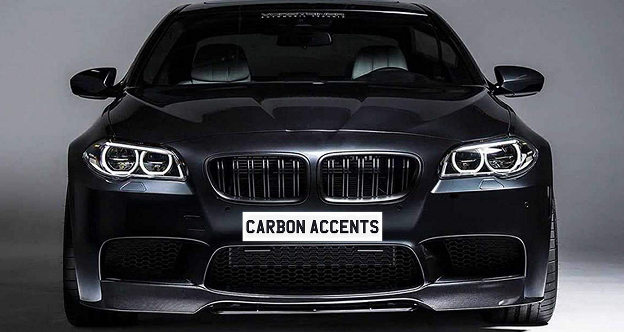 The car is a sleek black sedan with illuminated headlights facing forward. Text on the front reads "CARBON ACCENTS." It's positioned in a dimly lit studio environment.