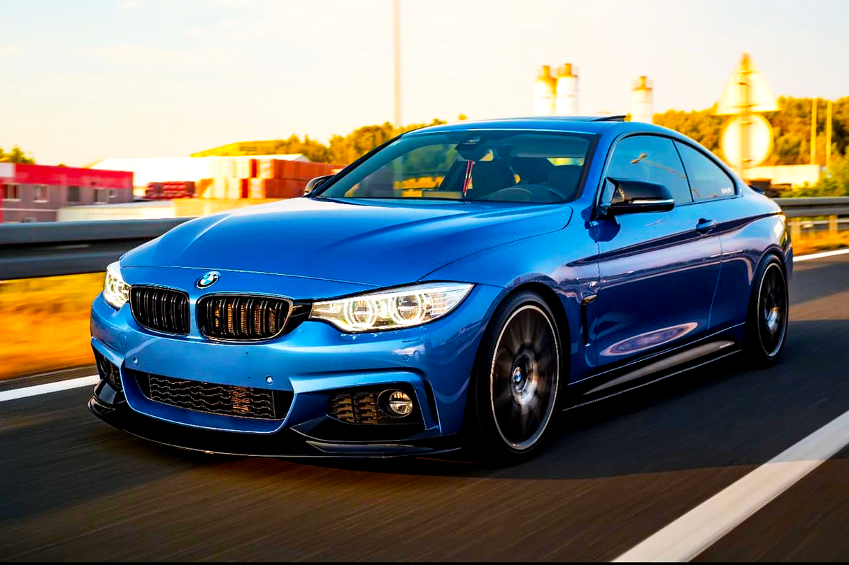 A blue sports car speeds along a highway, surrounded by blurred motion lines and distant industrial buildings in the background.