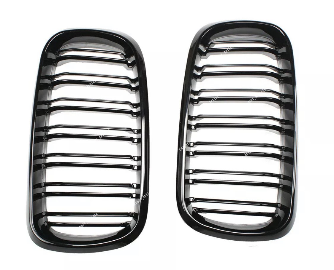 Two glossy black car grilles with horizontal slats are positioned side by side on a white background. Subtle reflections highlight their contours.