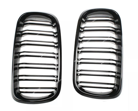 Two glossy black car grilles with horizontal slats are positioned side by side on a white background. Subtle reflections highlight their contours.