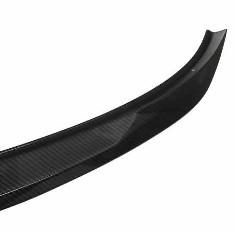 Curved carbon fiber car spoiler, resting on a plain white background, displaying a sleek design and a glossy surface texture.