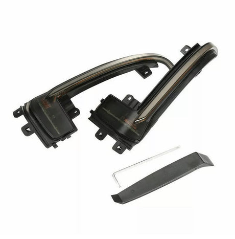 Two sleek, curved black car light covers with mounting brackets are placed on a white background. Below, a separate black trim piece and a small metal tool are included.