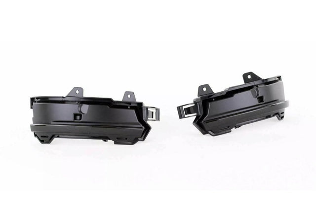 Two black plastic automotive parts, likely fog light housings, are positioned side by side facing outward. They feature mounting brackets and an angular design, set against a plain white background.
