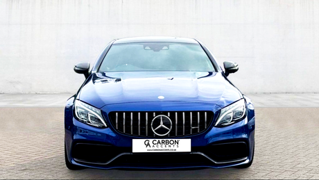A blue luxury car is parked on a paved surface, facing forward. Its front grille features a prominent emblem. The background is a plain, light-colored wall. Text reads: "CARBON ACCENTS, WWW.CARBONACCENTS.CO.UK."