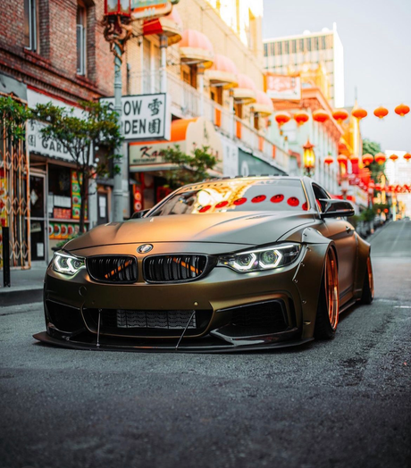 A sleek, customized BMW with lowered suspension parked on a street in Chinatown, surrounded by traditional architecture and red lanterns, creating a vibrant, urban setting.