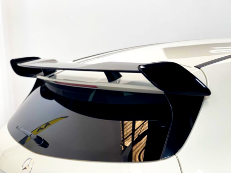 A sleek black car spoiler is mounted on the rear of a white vehicle, above a tinted back window with a visible wiper, in a well-lit indoor setting.