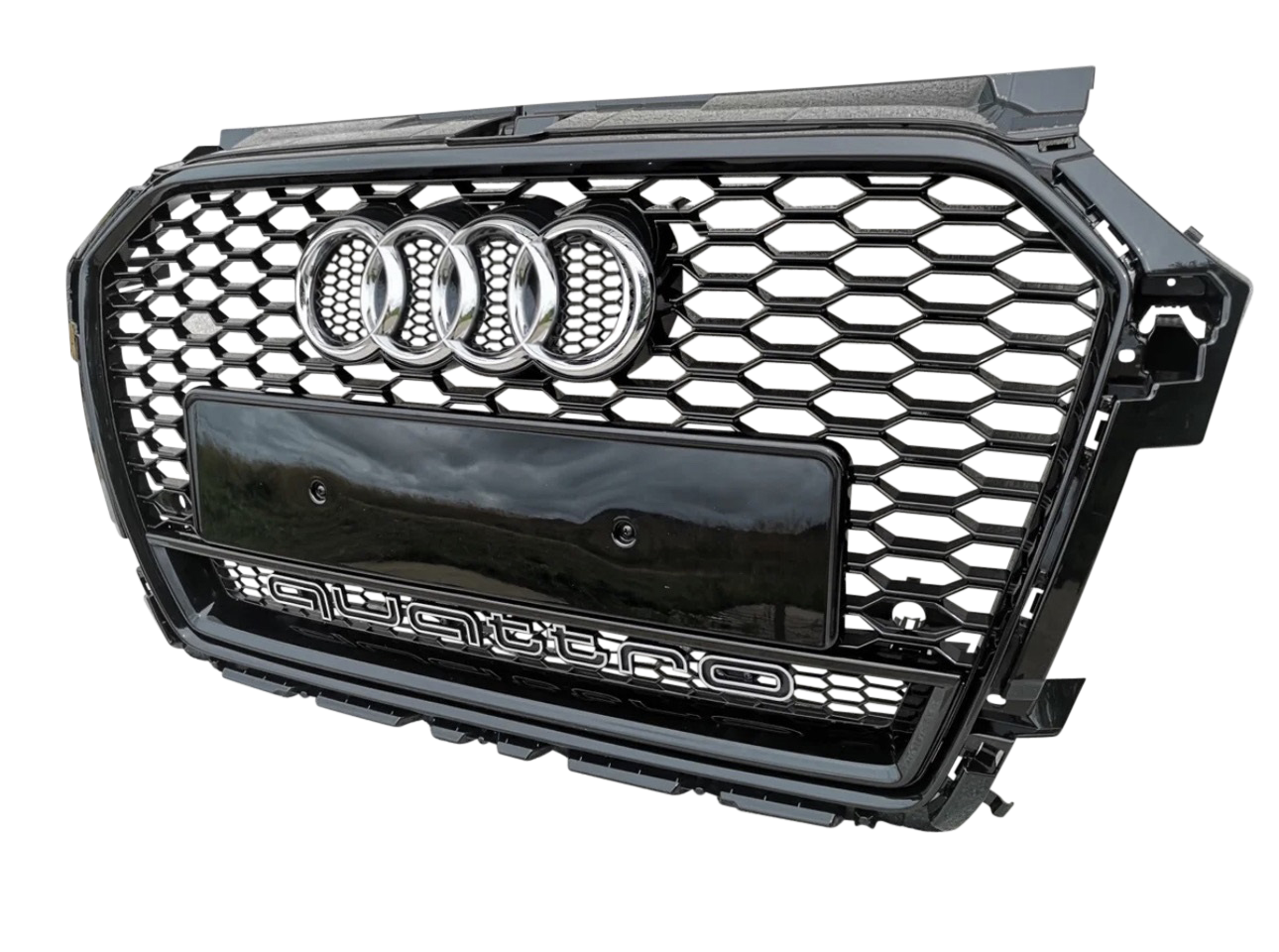 A black car grille with a honeycomb pattern, featuring four chrome rings and "quattro" text, is displayed against a plain background.