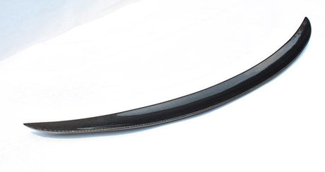 Curved carbon fiber car spoiler resting against a white background, showcasing its sleek, aerodynamic design.