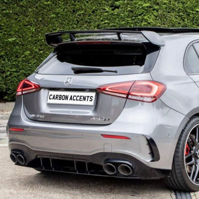 A silver Mercedes-Benz A250 has a prominent rear spoiler and dual exhausts, parked on a driveway with a hedge backdrop. The license plate reads "CARBON ACCENTS."