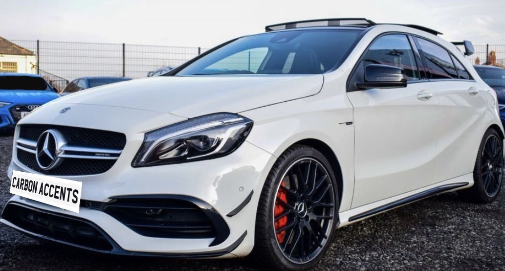 A white Mercedes-Benz car is parked on gravel, featuring black rims and red brake calipers. Other cars and a fence are visible in the background. The text reads "CARBON ACCENTS."