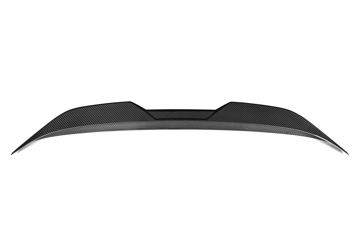 A sleek carbon fiber car spoiler sits against a white background, with a curved and aerodynamic design, featuring angular edges and textured surface details.