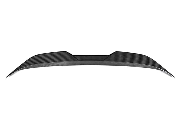 A sleek carbon fiber car spoiler sits against a white background, with a curved and aerodynamic design, featuring angular edges and textured surface details.