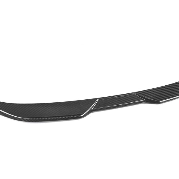 A sleek carbon fiber car spoiler with a subtle curve lies on a white background, highlighting its textured surface and aerodynamic design.