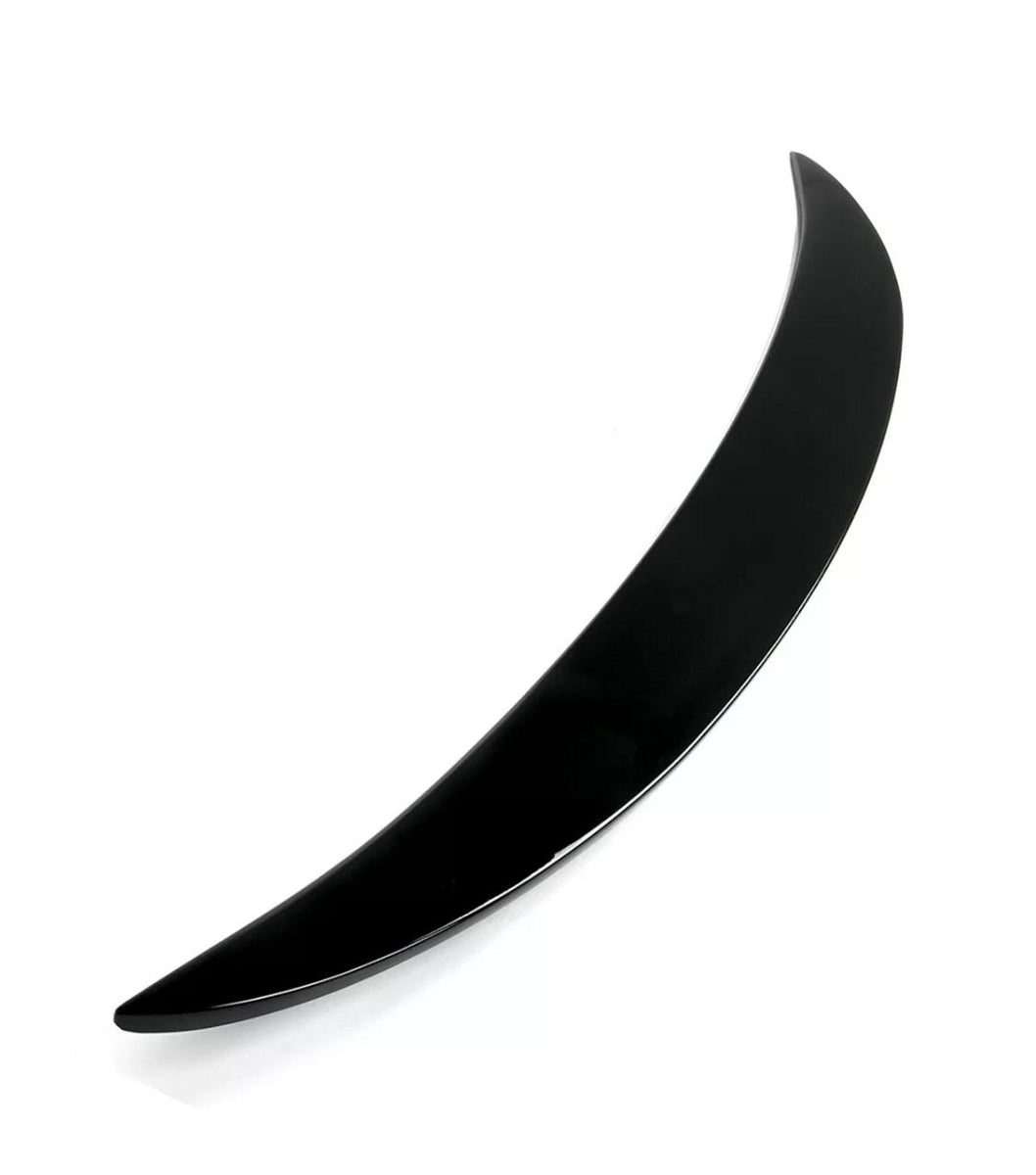 A sleek, curved black object, resembling a thin crescent, lies on a white surface. The object is glossy and tapers to a point at both ends.