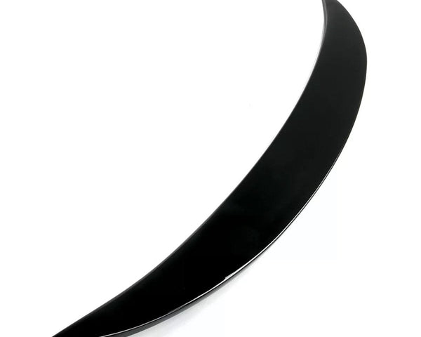 A sleek, curved black object, resembling a thin crescent, lies on a white surface. The object is glossy and tapers to a point at both ends.