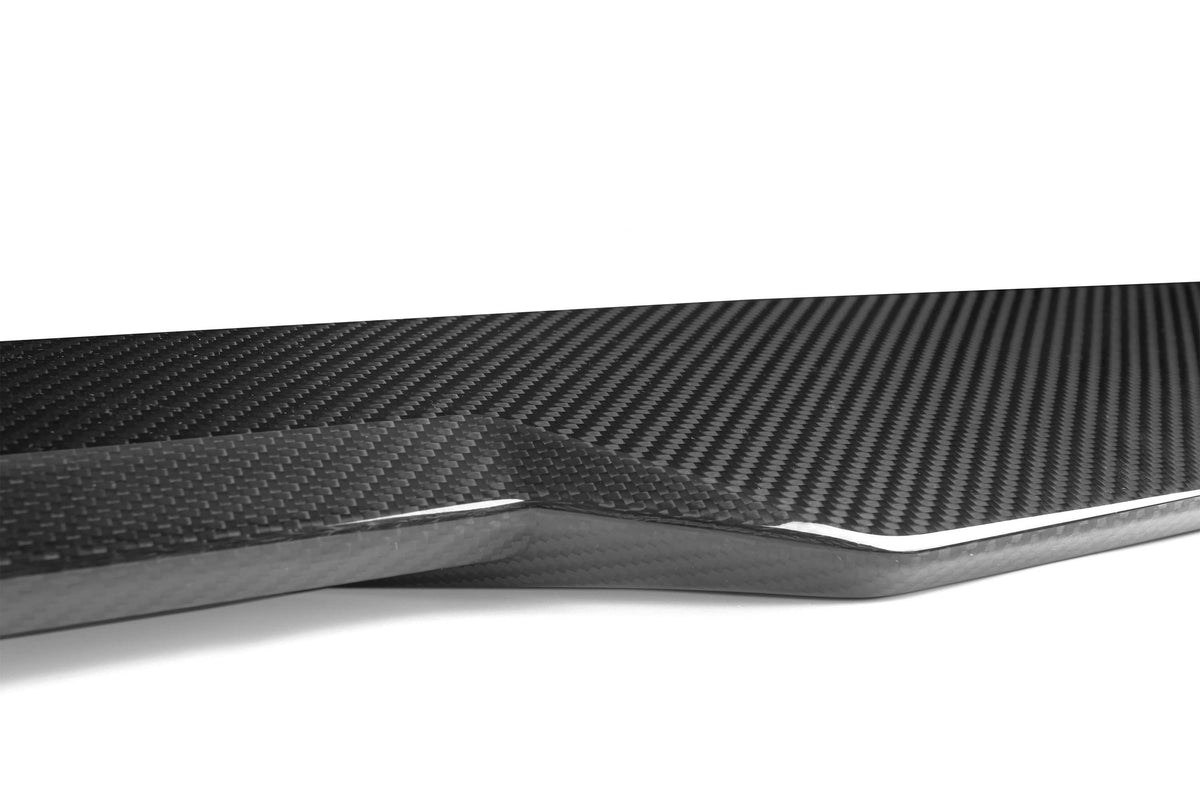 A sleek carbon fiber piece, displaying a glossy, woven texture, rests on a plain white background, emphasizing its modern design and intricate pattern.