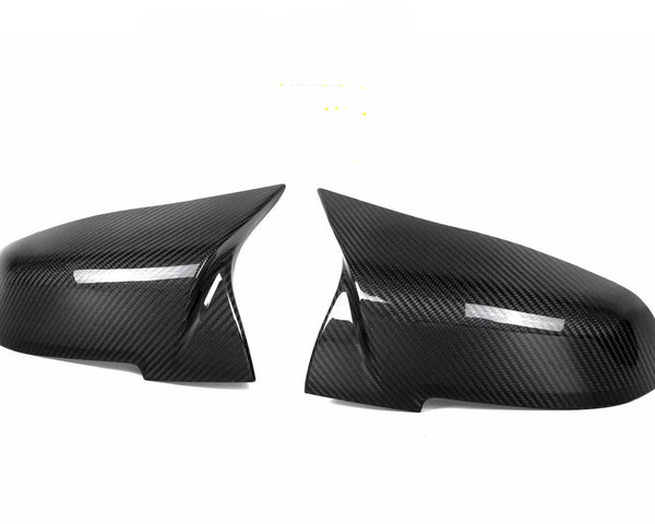 Two black carbon fiber side mirror covers are positioned facing each other against a plain white background, highlighting their sleek, aerodynamic design and glossy finish.