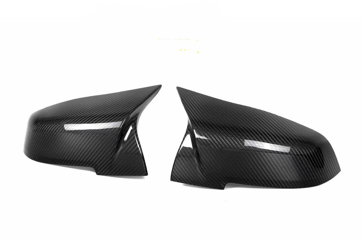 Two black carbon fiber side mirror covers are positioned facing each other against a plain white background, highlighting their sleek, aerodynamic design and glossy finish.