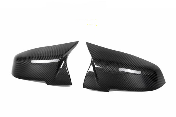 Two black carbon fiber side mirror covers are placed on a white background, showcasing their glossy, textured surface and aerodynamic design.