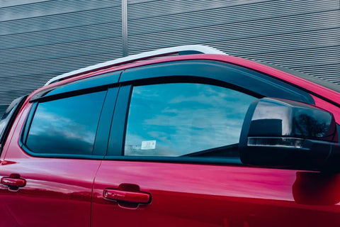 A red vehicle is parked with closed windows reflecting a cloudy sky. The background features a corrugated metal wall. A side mirror protrudes, and no text is visible.