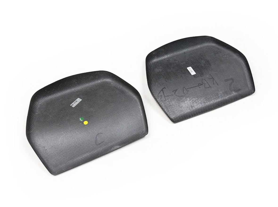 Two black, carbon-fiber plates lie on a white surface. The left plate is marked with dots and labeled "VENOM," while the right displays handwritten numbers.