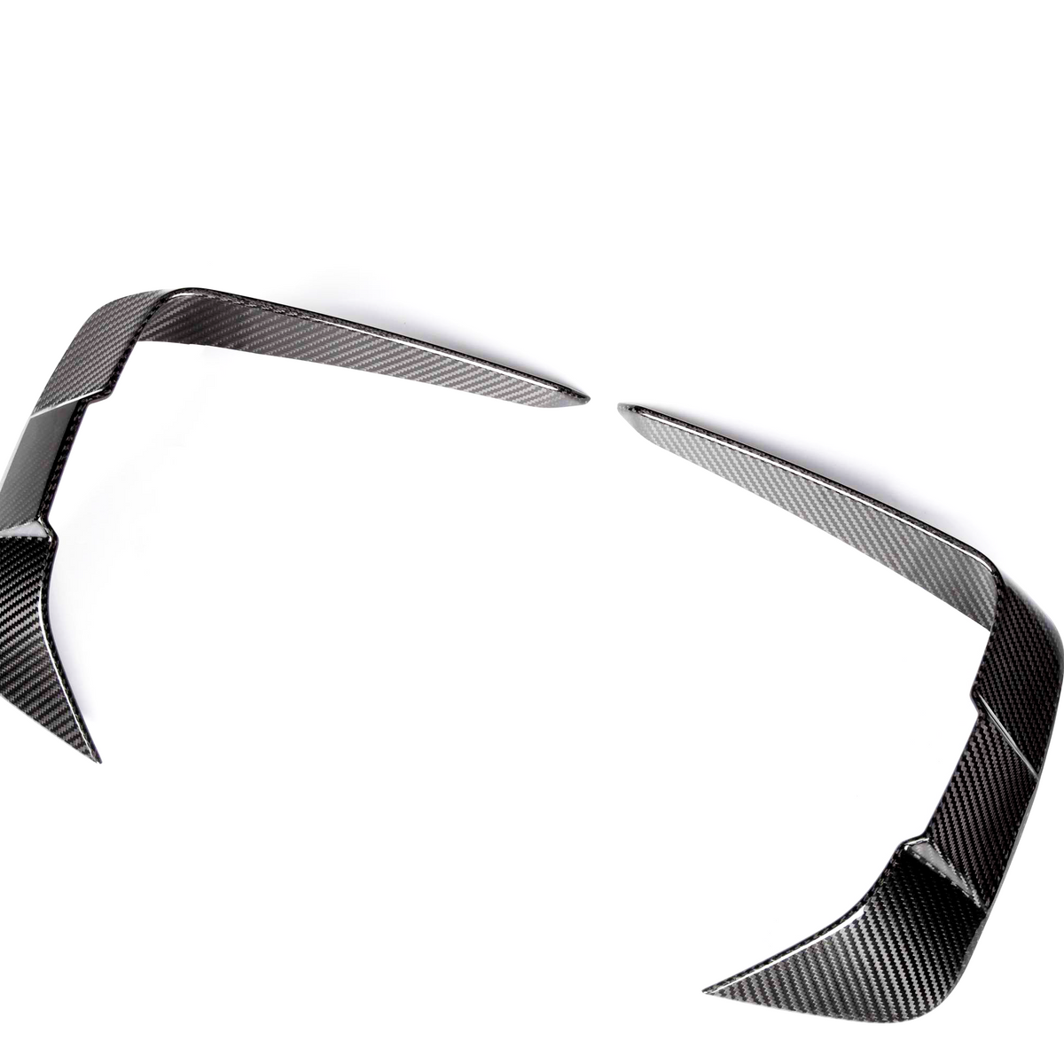 Curved carbon fiber car parts, resembling aerodynamic fins, rest apart on a white background, showcasing a sleek, reflective surface pattern.