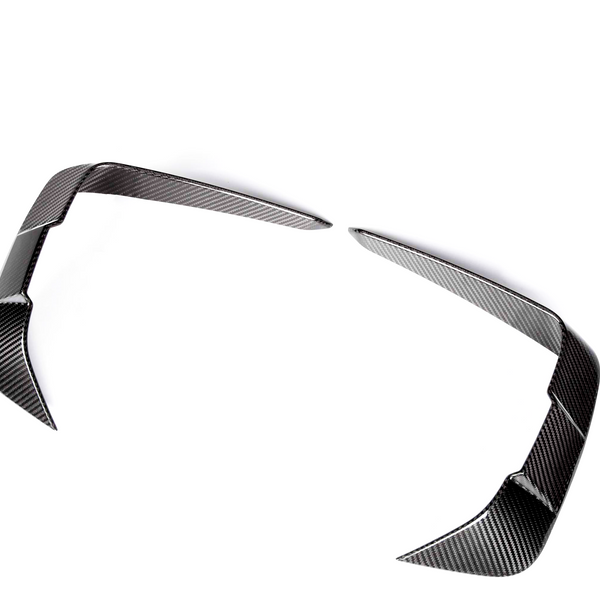 Curved carbon fiber car parts, resembling aerodynamic fins, rest apart on a white background, showcasing a sleek, reflective surface pattern.