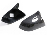 Two carbon fiber car mirror covers are displayed on a white background. One cover is upright, the other flipped, showing an internal barcode sticker.