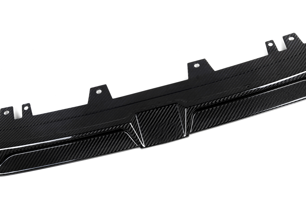 A carbon fiber car diffuser lies flat, showing textured pattern and mounting brackets, set against a plain white background.