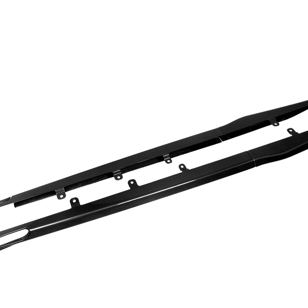 Two long, black carbon fiber side skirts with mounting brackets lie side by side on a plain white background. The word "Amuse" is visible on one end.