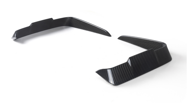 Two carbon-fiber vehicle splitters angled upward, placed on a white surface, likely designed for aerodynamics, showing a modern, sleek pattern.