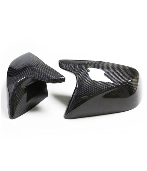 Two carbon fiber car mirror covers are placed on a white surface, reflecting light, showcasing a sleek, smooth texture and angular design.
