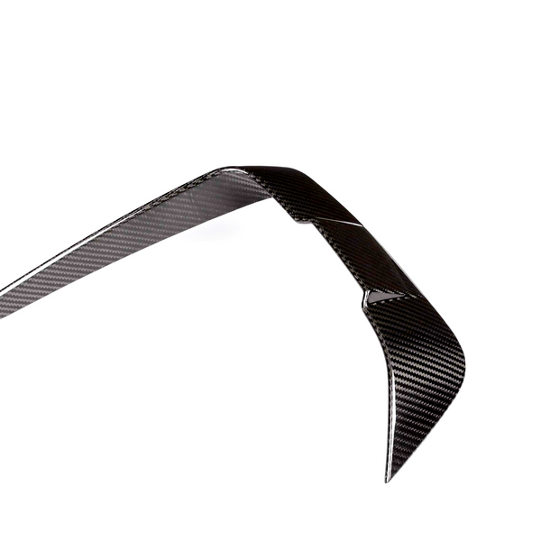 A shiny carbon fiber boomerang rests in a balanced, upright position against a plain white background, displaying a smooth, woven texture.