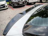 A glossy car, parked, reflects trees and sky on its rear window. Other vehicles are parked nearby in an outdoor lot.