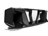 A carbon fiber car part with aerodynamic, angular features rests on a smooth white background, emphasizing its sleek, glossy finish and intricate texture.