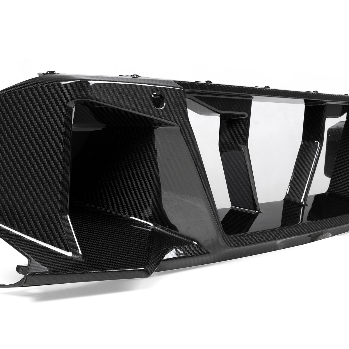 A carbon fiber car part with aerodynamic, angular features rests on a smooth white background, emphasizing its sleek, glossy finish and intricate texture.