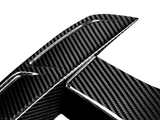 A close-up of a carbon fiber car spoiler, displaying a textured, woven pattern. The object is set against a plain white background, highlighting the material's glossy finish.