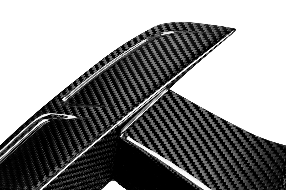 A close-up of a carbon fiber car spoiler, displaying a textured, woven pattern. The object is set against a plain white background, highlighting the material's glossy finish.
