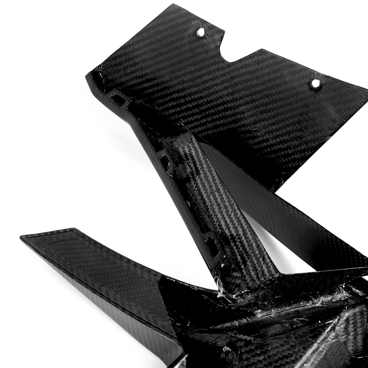 A carbon fiber automotive component with sleek, angular design lays on a plain white background, showcasing its lightweight and durable structure.